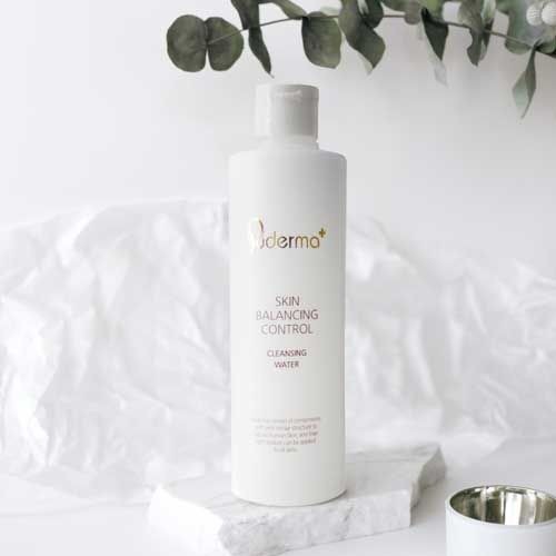 Bottle of skin balancing control cleansing water on a white surface with leaves in the background.