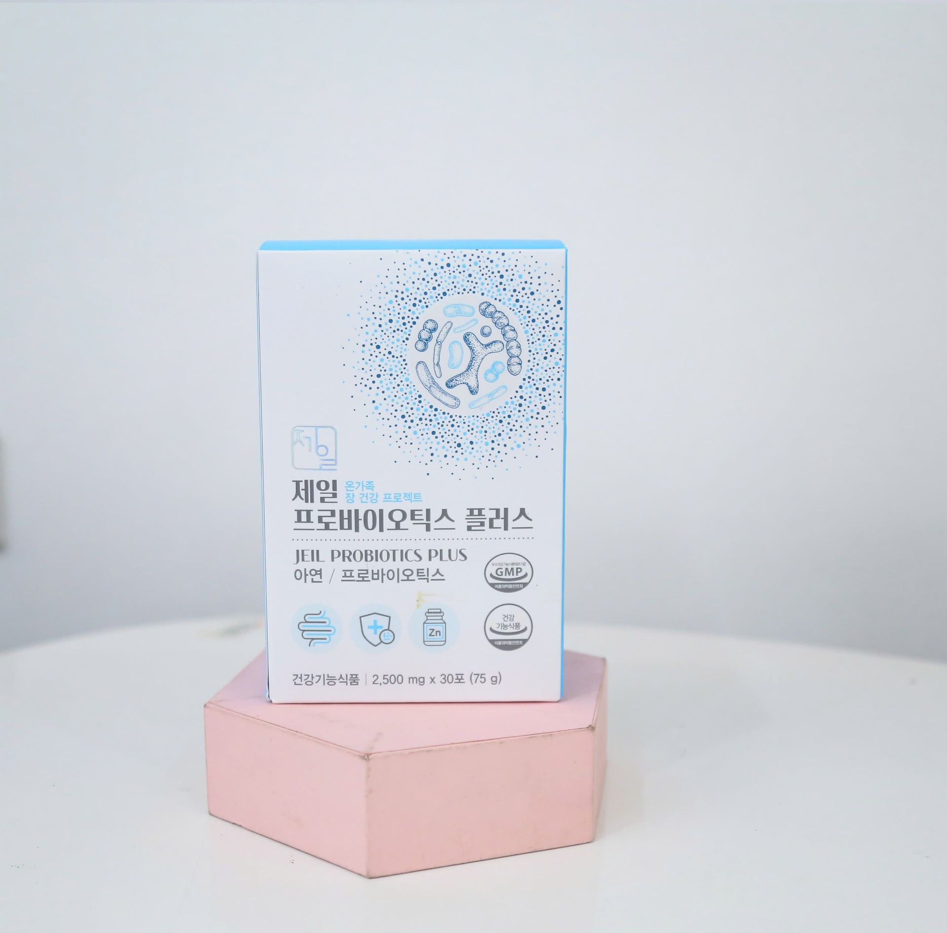 Box of Jeil Probiotics Plus supplement on a pink hexagonal stand against white background.