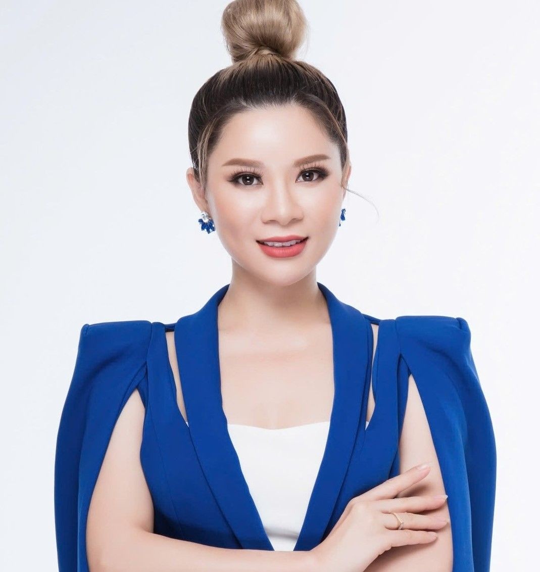 Woman in a blue dress with an elegant bun hairstyle and blue earrings, smiling at the camera.