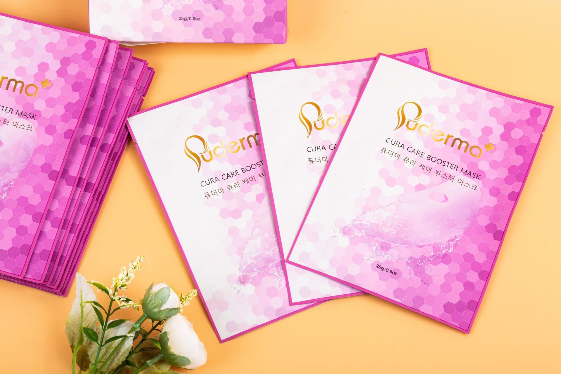 Pink hexagon-patterned face mask packages arranged on a peach background with white flowers.