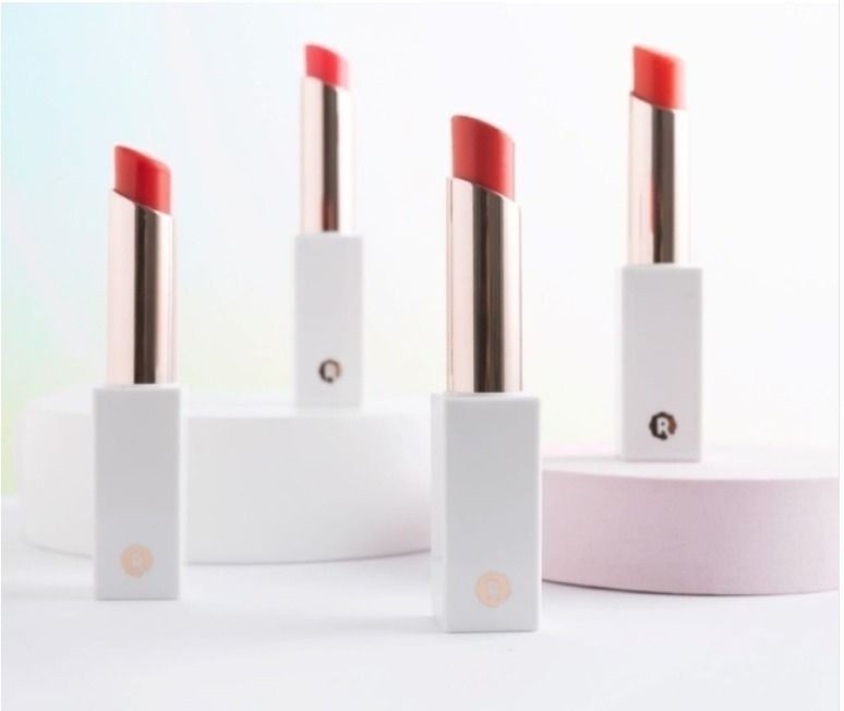 Four red lipsticks in white cases with gold accents on a light background.