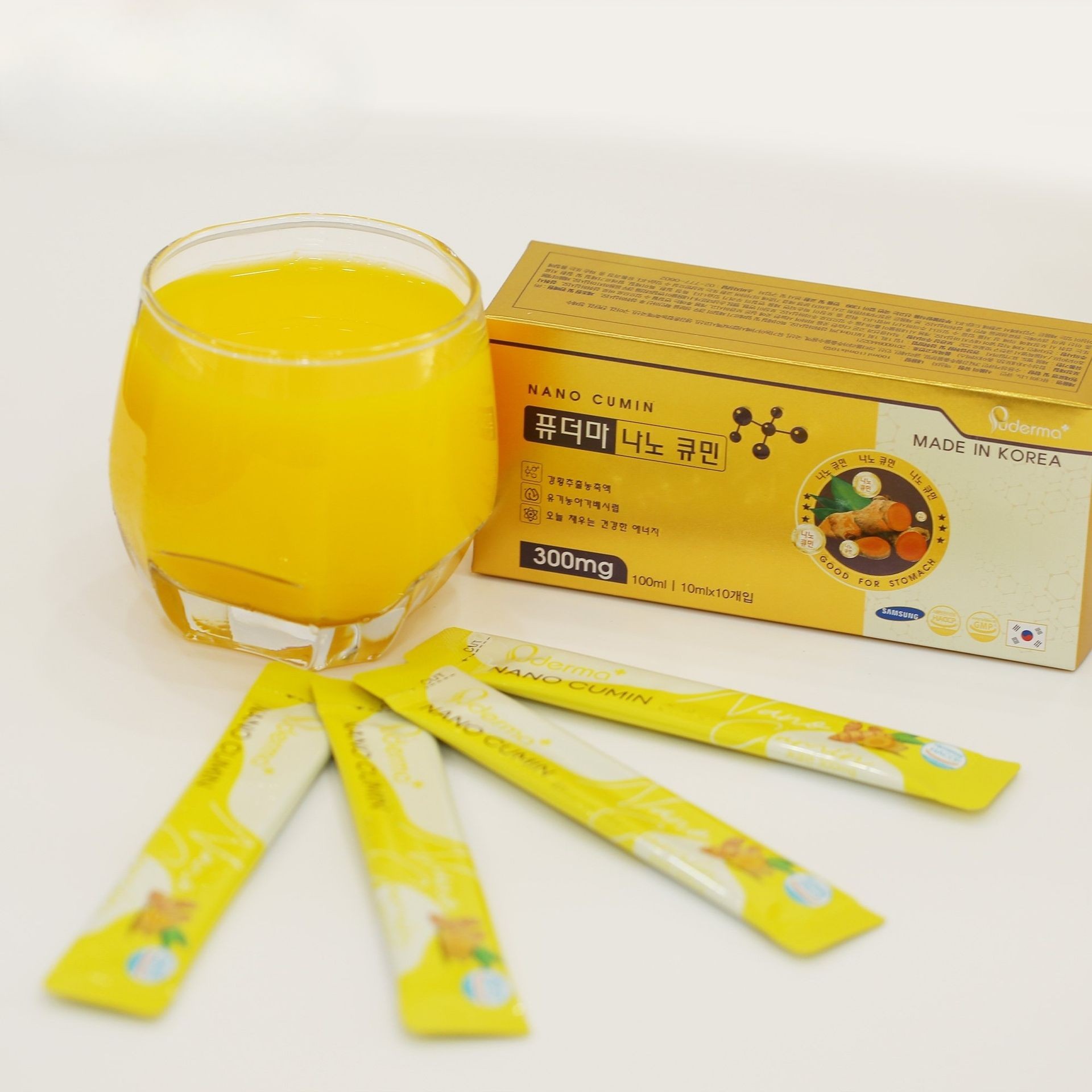 Glass of yellow liquid next to a box and packets of Korean-made Nano Cumin powder.